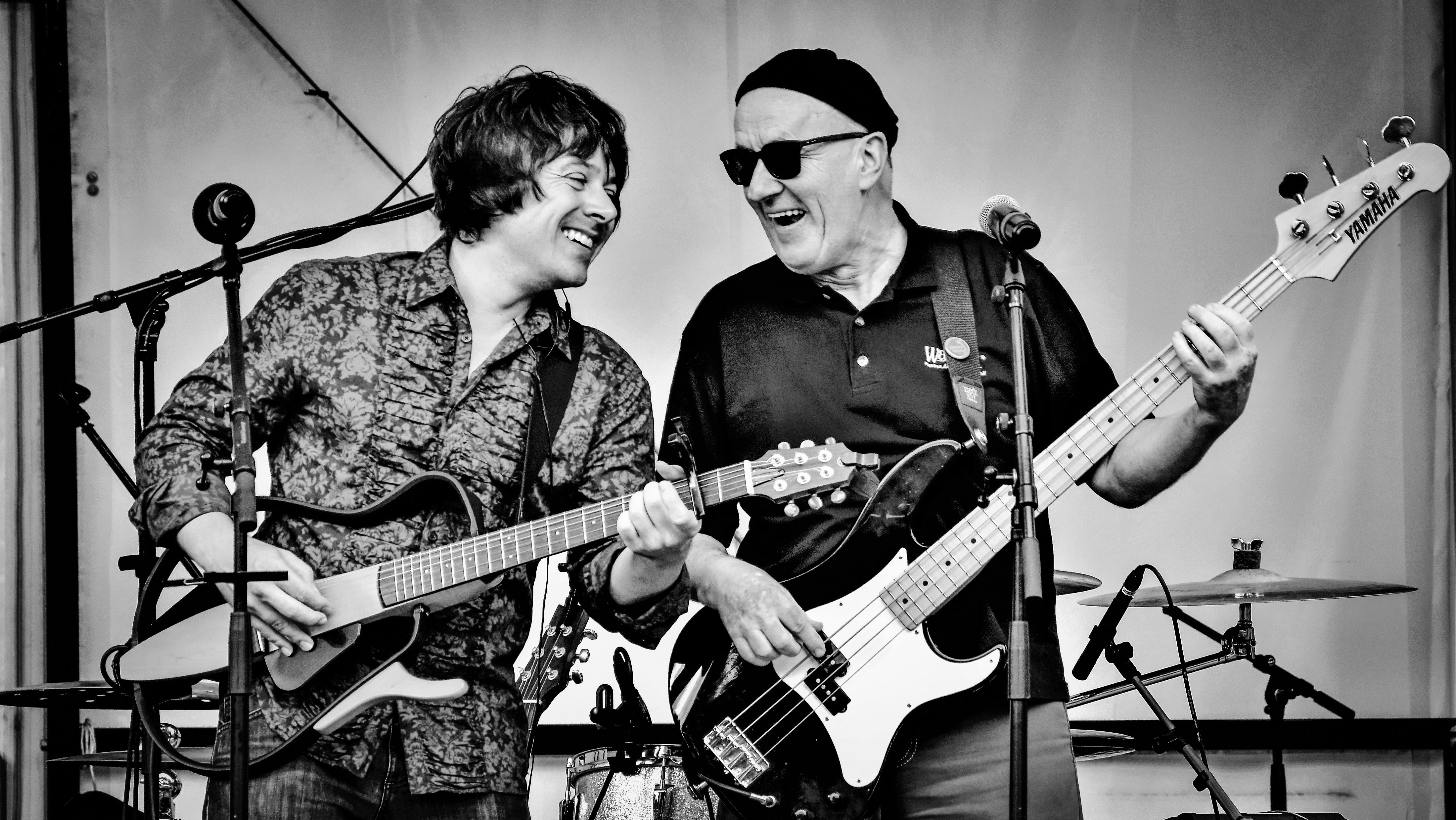 Two musicians Leon and Thommi performing on stage, one playing guitar and the other playing bass, both smiling and enjoying the music.